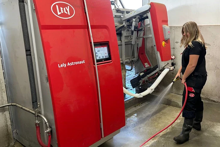 person rinsing down lely machine with water hose